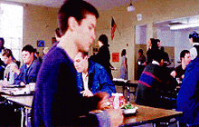 a group of people are sitting at tables in a cafeteria eating food