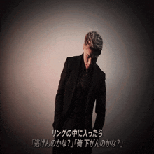 a man in a suit stands in front of a wall with japanese writing