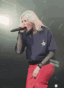 a woman singing into a microphone while wearing a shirt with a star on it