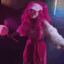a woman with pink hair and a hat is dancing in a club .
