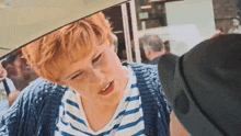 a woman with red hair and a striped shirt is talking to a man .