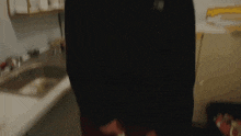 a person in a black shirt is standing in front of a sink in a kitchen