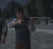 a man in a vest is holding a gun in a field with trees in the background