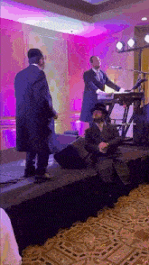 a man in a hat is sitting on a stage while another man plays a keyboard .