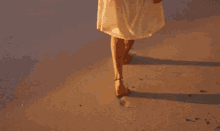 a woman in a white dress is walking on a beach