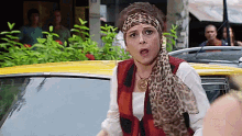 a woman wearing a leopard print scarf is standing in front of a car .