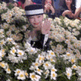 a man in a hat stands in front of a bunch of white flowers