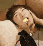 a young man is laying on a couch eating a piece of food with a fork in his mouth .