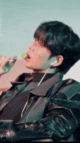 a man wearing ear buds and a leather jacket is eating a lollipop