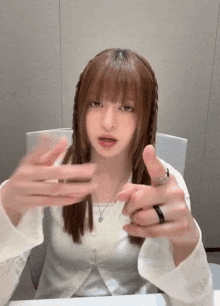 a young woman is sitting at a table with her hands outstretched and pointing at the camera .