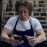 a man wearing an apron and a white shirt looks at his phone
