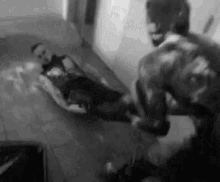 a black and white photo of a man laying on a bed with another man standing next to him .