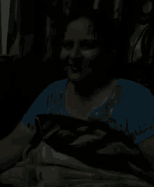 a woman in a blue shirt is laying under a blanket in the dark and smiling .