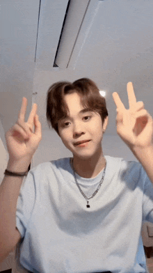 a young man in a blue shirt is making a peace sign with both hands