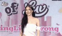 a woman in a white off the shoulder dress is standing in front of a pink sign .