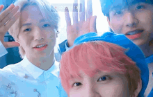 a group of young men with pink hair are standing next to each other and waving at the camera .