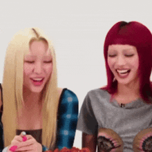two women with blonde hair and red hair are sitting next to each other smiling
