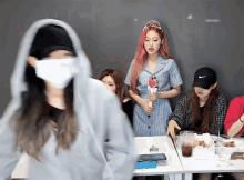 a group of girls are sitting at a table and one of them is wearing a mask