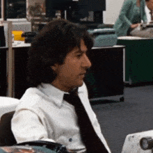 a man in a white shirt and black tie is sitting in an office