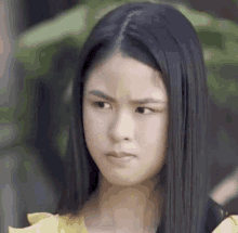 a young woman with long black hair is making a funny face and wearing a yellow shirt .