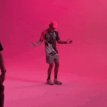 a man is standing in front of a pink wall with his arms outstretched and wearing a hat .