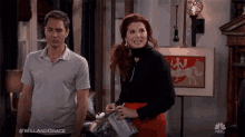 a man and a woman are standing in a living room with the hashtag #willandgrace on the bottom right