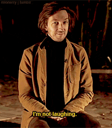 a man in a brown jacket and black turtleneck is sitting down and says i 'm not laughing