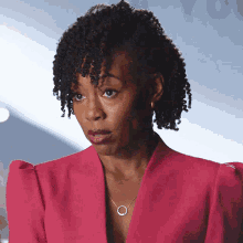 a woman with curly hair is wearing a pink jacket and a silver necklace