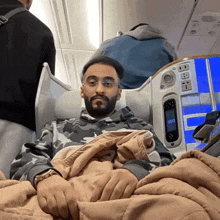 a man sitting on an airplane with a blanket and a display that says 10:08 on it