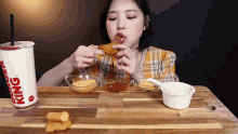 a woman is sitting at a table eating chicken nuggets and a burger king drink