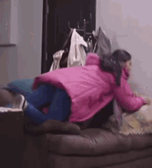 a girl in a pink coat is laying on a couch with a dog .