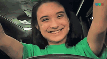 a girl in a green shirt is smiling with her arms up