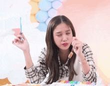 a woman is holding a brush in her hand while sitting at a table with balloons in the background .