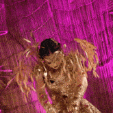 a woman in a gold dress is standing in front of a purple wall .