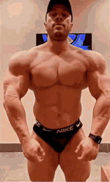 a very muscular man is standing in a gym wearing nike underwear and a hat .