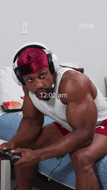 a man wearing headphones sits on a bed at 12:02 am in 2018