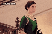 a woman in a green saree is standing on a staircase .