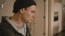 a man wearing a black beanie and a grey sweatshirt looks down