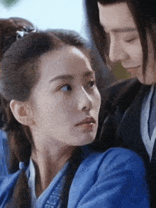 a man and a woman are looking at each other with their eyes closed . the woman is wearing a blue dress .