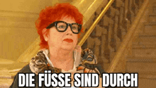 a woman with red hair and glasses is sitting on a set of stairs with the words `` die fusse sind durch '' .