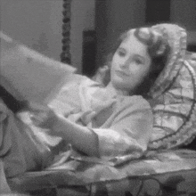 a black and white photo of a woman laying on a bed reading a book