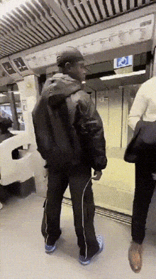 a man in a black jacket is standing in a subway