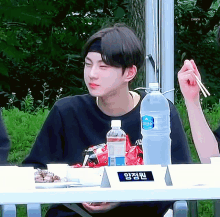 a young man is sitting at a table with a bottle of water and a sign that says ' check ' on it