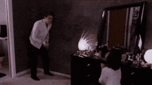 a man is standing next to a woman sitting in front of a dresser in a room .