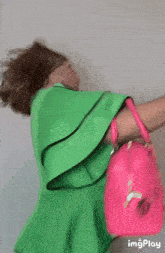 a woman in a green top is holding a pink purse .