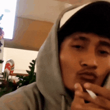 a man wearing a hat and a hoodie smoking a cigarette