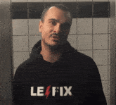 a man in a black le fix hoodie stands in front of a tiled wall