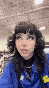 a girl with black hair and a nose ring is wearing a blue jacket and earrings .