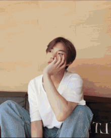 a young man in a white shirt sits on a couch with his hand on his face