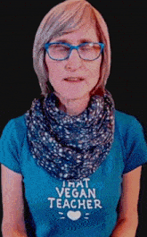 a woman wearing glasses and a scarf is wearing a t-shirt that says that vegan teacher